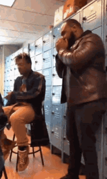 two men are standing in front of lockers in a room .
