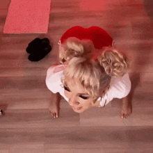 a woman is doing push ups on the floor while wearing a white shirt and red shorts .