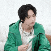 a young man wearing a green jacket holds a piece of paper in his hand