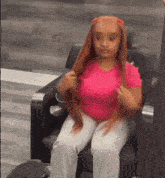 a young girl in a pink shirt is sitting in a chair