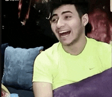 a young man wearing a neon yellow nike shirt is sitting on a couch .