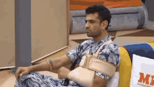 a man with a broken arm is sitting on a couch with a bandage on his arm .