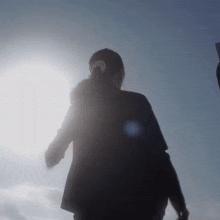 a woman in a black jacket stands in the sunlight