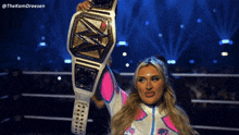 a woman in a pink and white outfit is holding up a wrestling belt