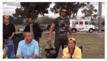 a group of people are standing in a park with a white truck in the background .