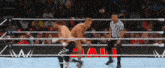 a referee is standing in the middle of a wrestling ring watching two men wrestle .