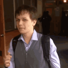 a young man wearing a vest and a backpack is walking down a hallway