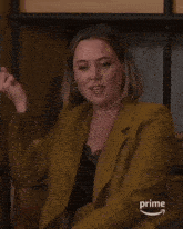 a woman in a yellow suit is sitting in front of a shelf that says prime on it