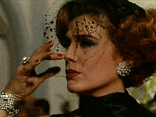 a woman wearing a veil and earrings holds her hand to her nose