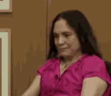 a woman in a pink shirt is sitting in front of a wooden wall and making a funny face .