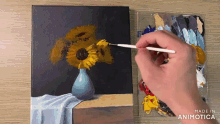 a person is painting a vase of sunflowers on a table