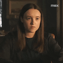 a woman is sitting in a chair and looking at the camera with a max logo in the background .