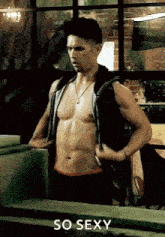 a man without a shirt is standing in front of a window .