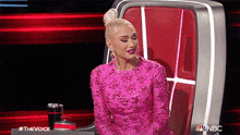 a woman in a pink dress is sitting in a red chair on a stage .