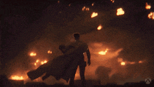 a man in a cape stands in front of a fire