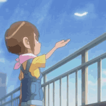 a little girl is standing on a balcony reaching up towards a white feather in the sky .