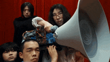 a group of people are standing in front of a red curtain while a woman holds a megaphone