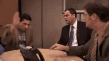 three men are sitting around a table with one wearing a t-shirt that says duke on it