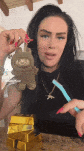 a woman is holding a stuffed animal and a toothbrush in front of a stack of gold bars