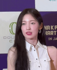 a woman with long black hair wearing a white shirt and earrings is standing in front of a purple wall .