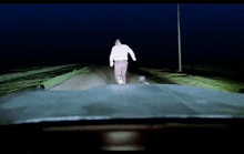 a man in a white sweater is walking down a road at night