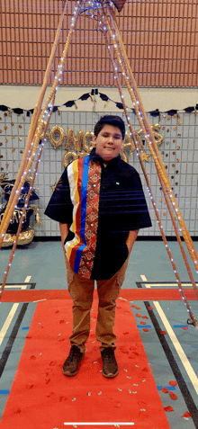 a boy is standing on a red carpet in front of a teepee