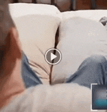 a person is sitting on a bed with their legs crossed and a play button .