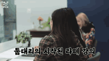 a woman sitting at a desk with twice written on the bottom of the screen