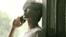 a young man leans against a wall while talking on a cell phone