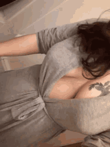 a woman in a grey dress has a tattoo on her shoulder