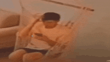 a blurry picture of a man sitting on a couch looking at his phone .