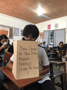 a man sitting in a classroom holding a bag that says yung crush ko nga di ko makuha perfect score pa kaya