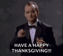 a man in a tuxedo is holding a glass of whiskey and says have a happy thanksgiving .