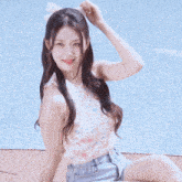 a woman in a white top and blue shorts sits in front of a swimming pool