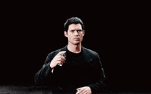 a man in a black suit and black t-shirt is looking at the camera .