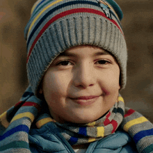 a young boy wearing a striped hat and scarf is smiling
