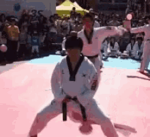 a group of people are practicing martial arts on a pink mat in front of a crowd .