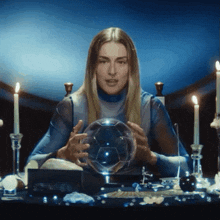 a woman is sitting at a table with candles and a crystal ball