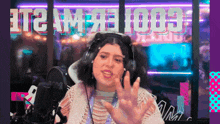 a woman wearing headphones stands in front of a microphone in front of a neon sign that says ' cool '