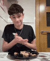a boy wearing a nike shirt sits at a table with a plate of food on it