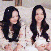 two young women are sitting next to each other on a couch and smiling .