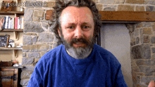 a man with a beard wearing a blue shirt is standing in front of a stone wall with the hashtag @itsscottiesstark