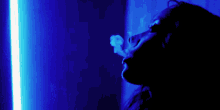 a woman is smoking a cigarette in a dark room with a blue light behind her