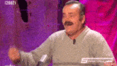 a man with a mustache is sitting in front of a microphone and making a funny face .