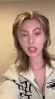 a woman with long blonde hair is wearing a white sweater with the letter t on it .