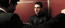 a man in a black leather jacket talks to another man in a suit