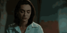 a woman in a white shirt and earrings is standing in a dark room and looking at the camera .