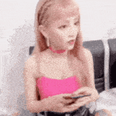 a woman in a pink top is sitting on a couch looking at her phone .