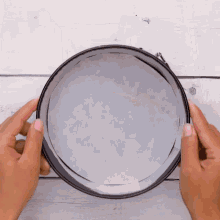 a person is holding a cake pan on a white wooden table