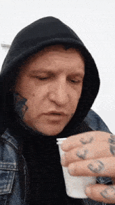 a man with a tattoo on his face is drinking from a white cup